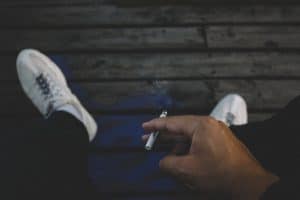 Fumeurs, préparez vous à payer plus chers vos crédits et assurances, des montants astronomiques réellement dissuasifs A man casually smoking a cigarette while relaxing outdoors on a wooden deck.