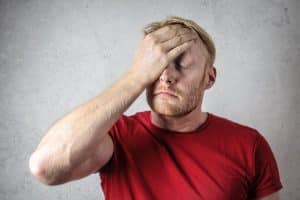 Fonctionnaires en danger : cette décision radicale qui baisse drastiquement leur salaire et ébranle le pays A frustrated man in a red shirt holds his head in stress against a neutral background.