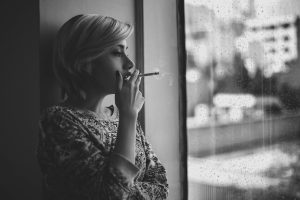 3 raisons de ne surtout pas interdire les sachets de nicotine Black and white depressed female with short haircut smoking cigarette and looking out window at rainy city