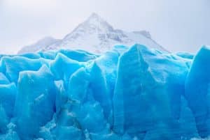 A stunning view of a vibrant blue glacier set against snow-capped mountains, showcasing winter's beauty.