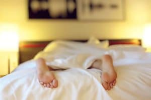 Ce phénomène troublant : découvrez pourquoi vous vous réveillez toujours avant votre alarme, vous n’en reviendrez pas A person relaxing on a bed with feet under white sheets, conveying serenity.
