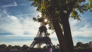 Eiffel Tower peeked by sunlight through trees in a Paris cityscape.