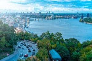 A vibrant skyline and river view of Kyiv, Ukraine, showcasing urban architecture and traffic.