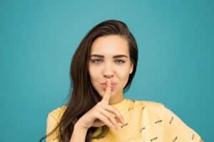 Selon Le Canard enchaîné, les anciens journalistes du groupe Bolloré seraient condamnés au silence Portrait of a woman with brown hair posing with a hush gesture against a blue background.
