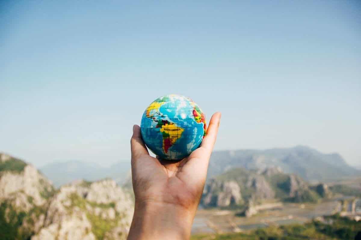 Les top destinations incontournables pour voyager en décembre Hand holding a globe against a mountain background symbolizing travel and exploration.