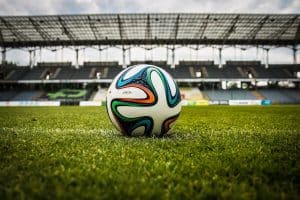 Quelle est l’importance des bonnes chaussures pour votre toucher de balle ? A vibrant soccer ball rests on a lush green field inside an empty stadium, capturing the essence of sports.