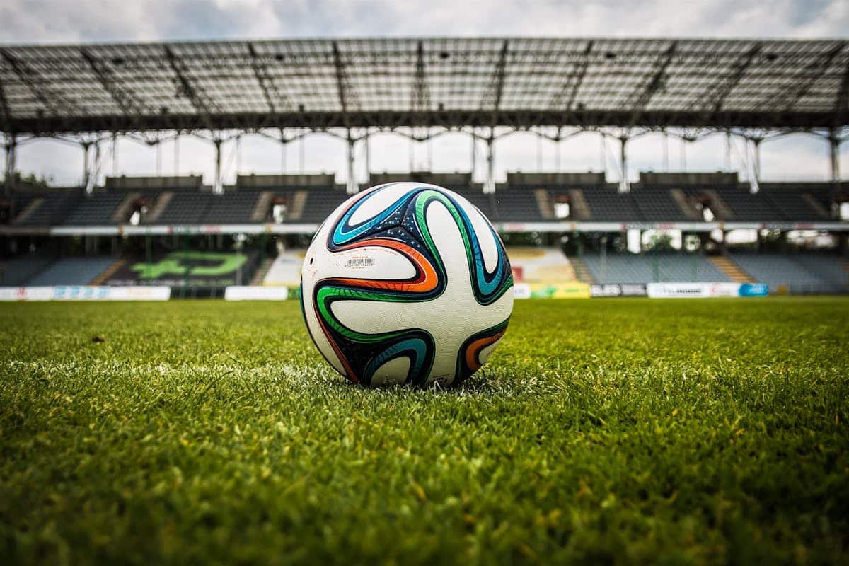 Quelle est l’importance des bonnes chaussures pour votre toucher de balle ? A vibrant soccer ball rests on a lush green field inside an empty stadium, capturing the essence of sports.