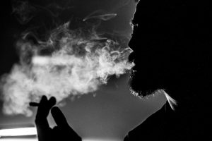 Choisir sa cigarette électronique : les recommandations indispensables d’un expert Dramatic black and white photo of a man's silhouette exhaling smoke, creating an atmospheric effect.