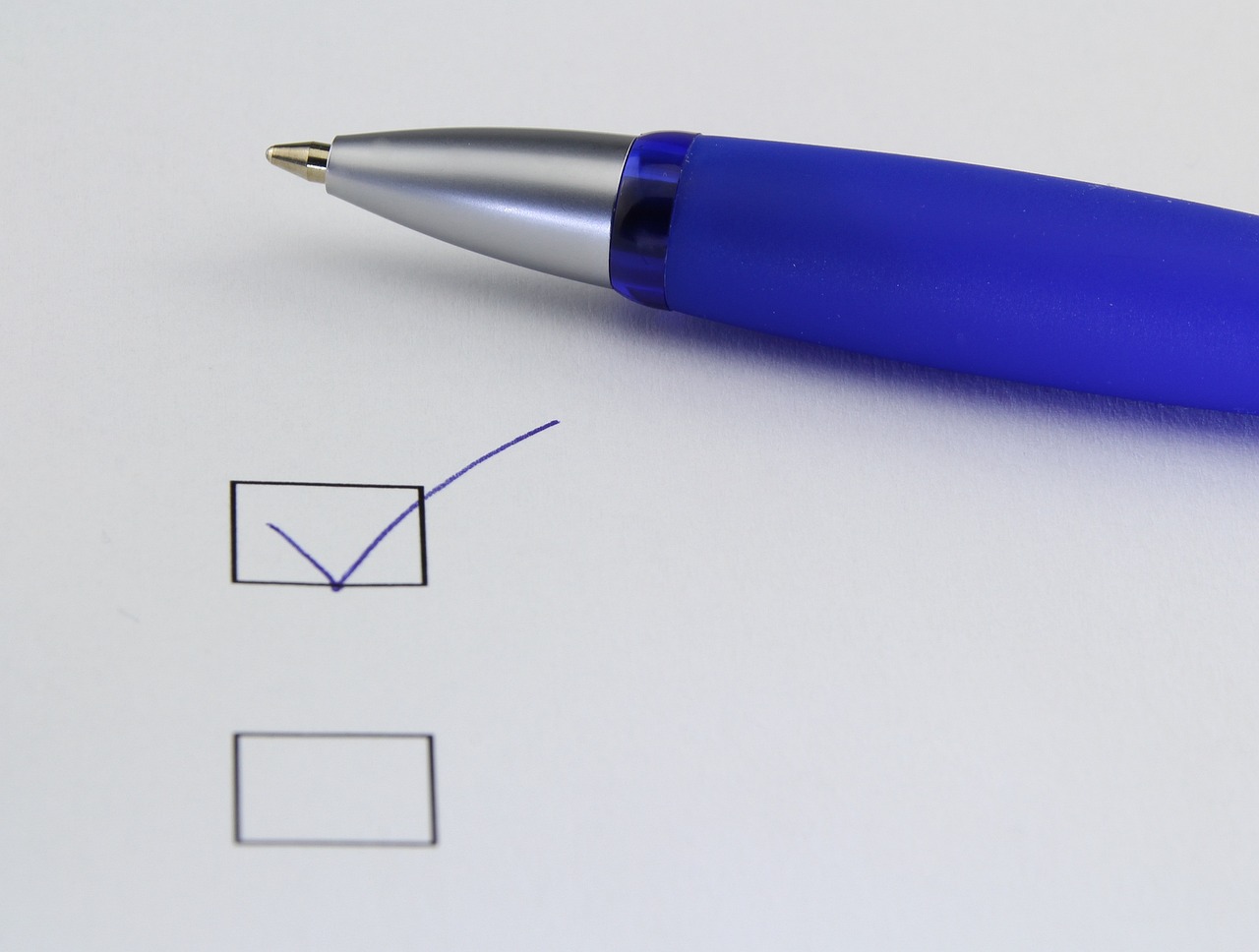 Stylo bleu au-dessus d'une case cochée et d'une case vide sur une feuille blanche